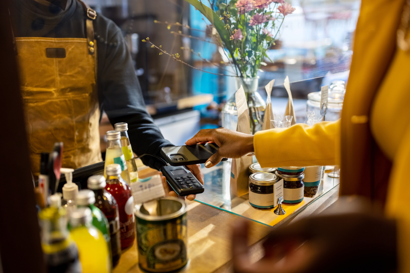 Cropped shot of a female customer using a smartphone for contactless payment. Cafe owner and customer at the checkout counter in a coffee shop.